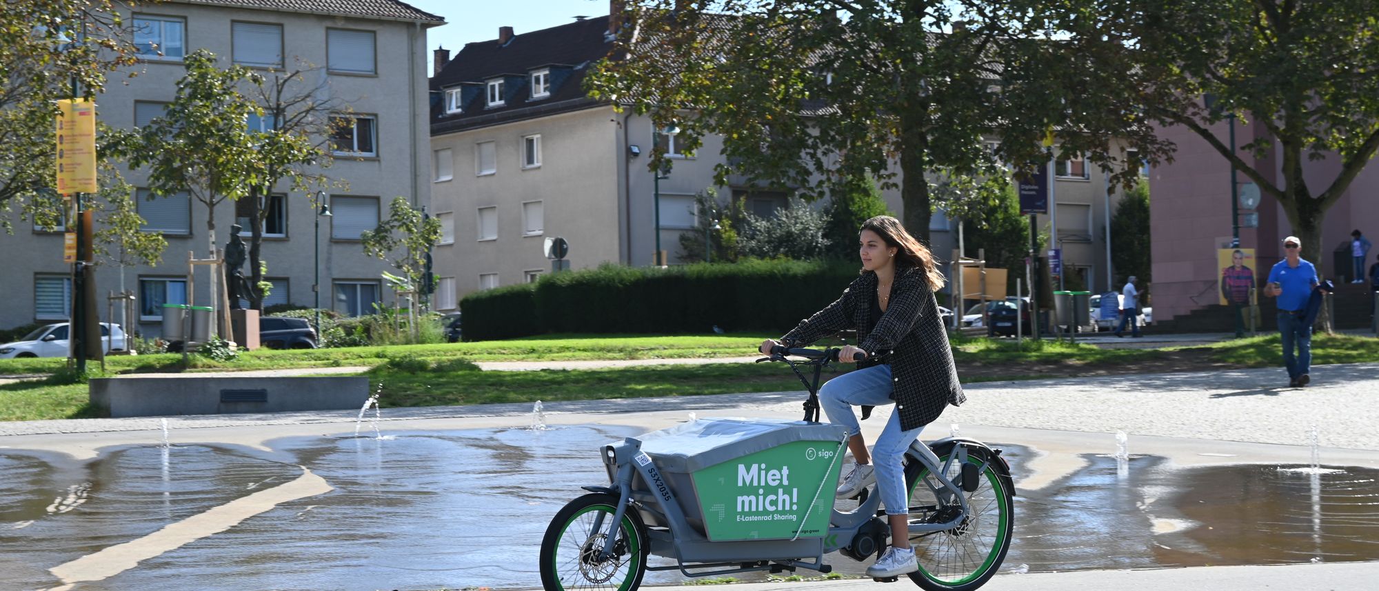 A rider crossing an urban square on a sigo e-cargo bike, with residential buildings behind