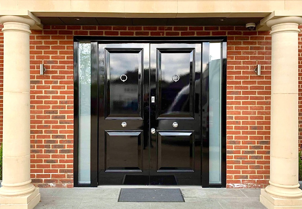 A porch with re bricks and a black double front door.