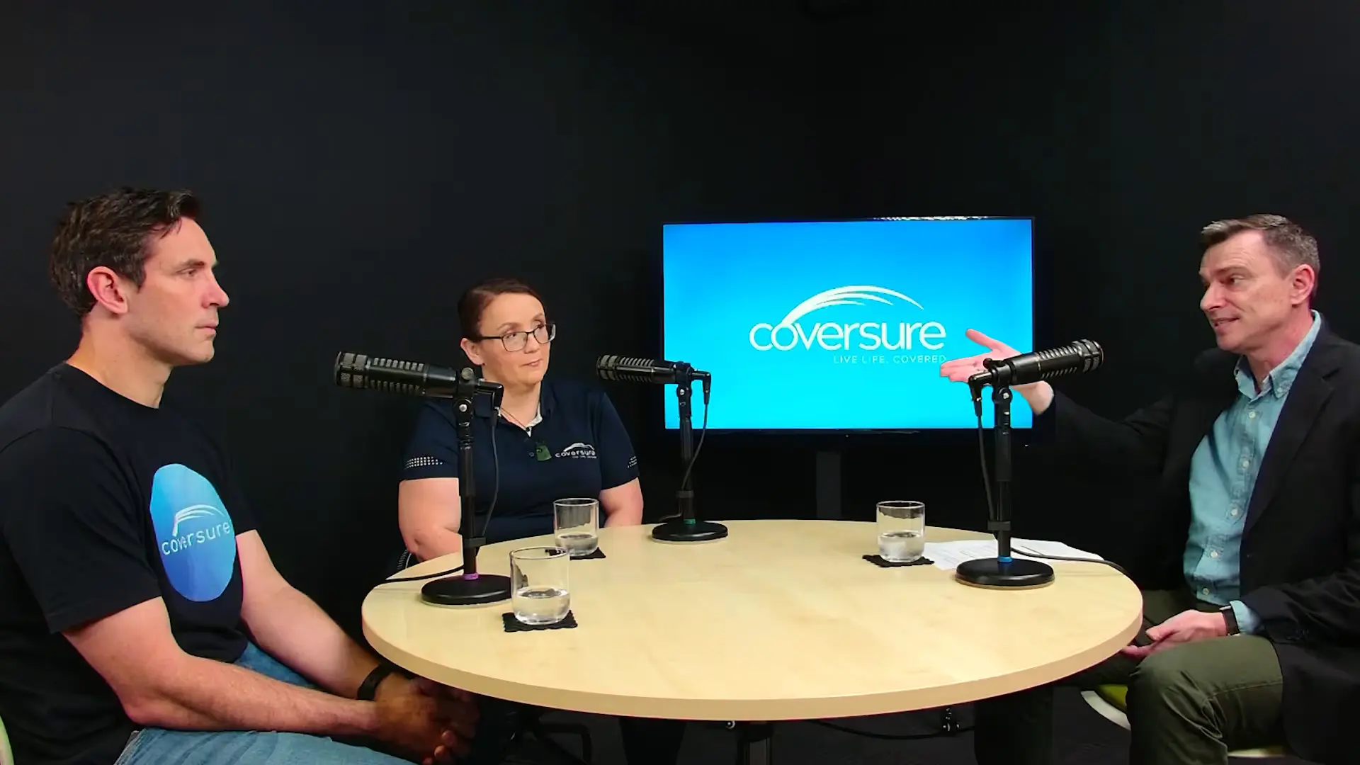 Three people sitting around a table with microphones, a screen displays Coversure logo behind them.