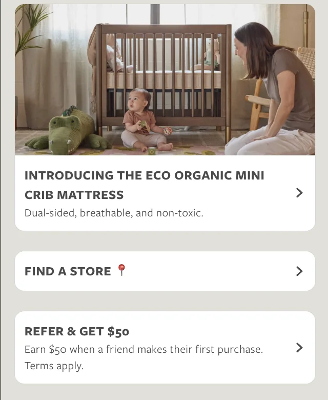 Baby sitting on floor playing near crib with woman kneeling, and a large green stuffed crocodile nearby.