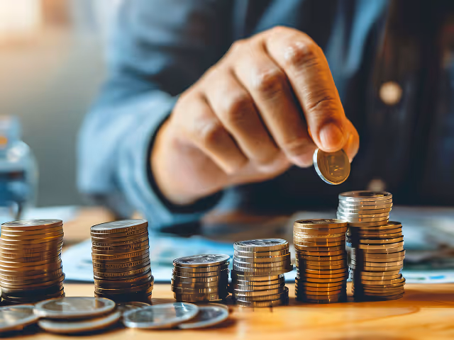 Person stacking coins in neat piles on a wooden surface with a blurred background.
