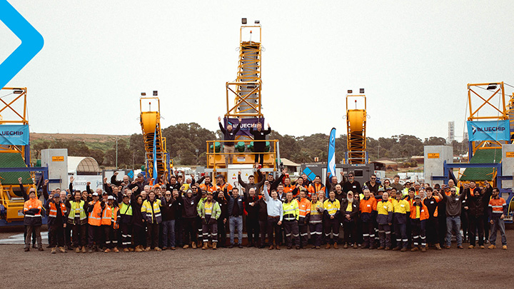Group of workers in high-visibility clothing standing in front of yellow stacker units