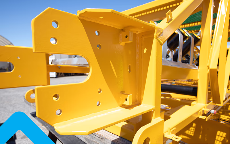 Yellow painted steel bracket with bolt holes, standing on a pallet outdoors