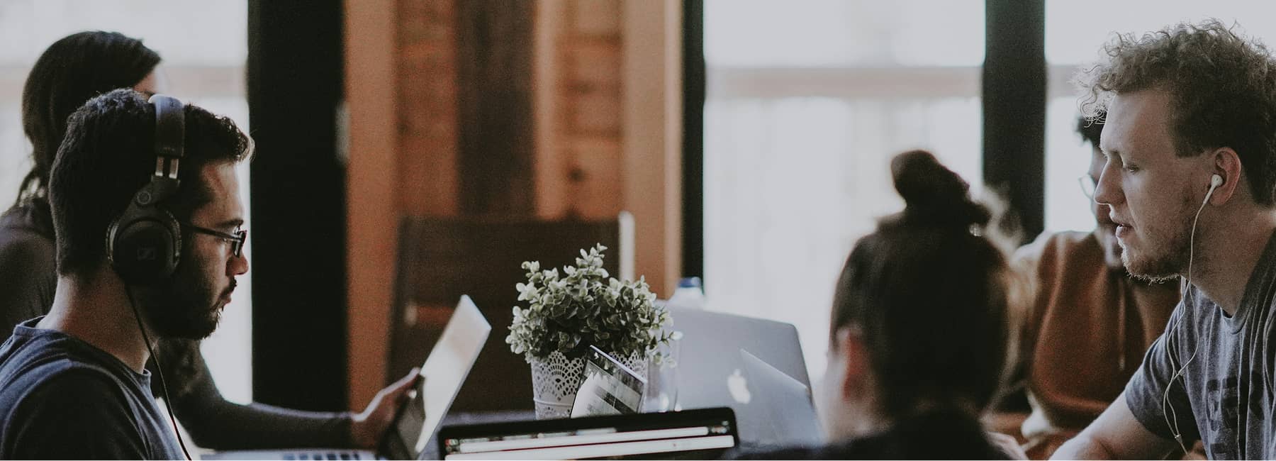 Group of young people working on laptops at a table in a casual office environment.