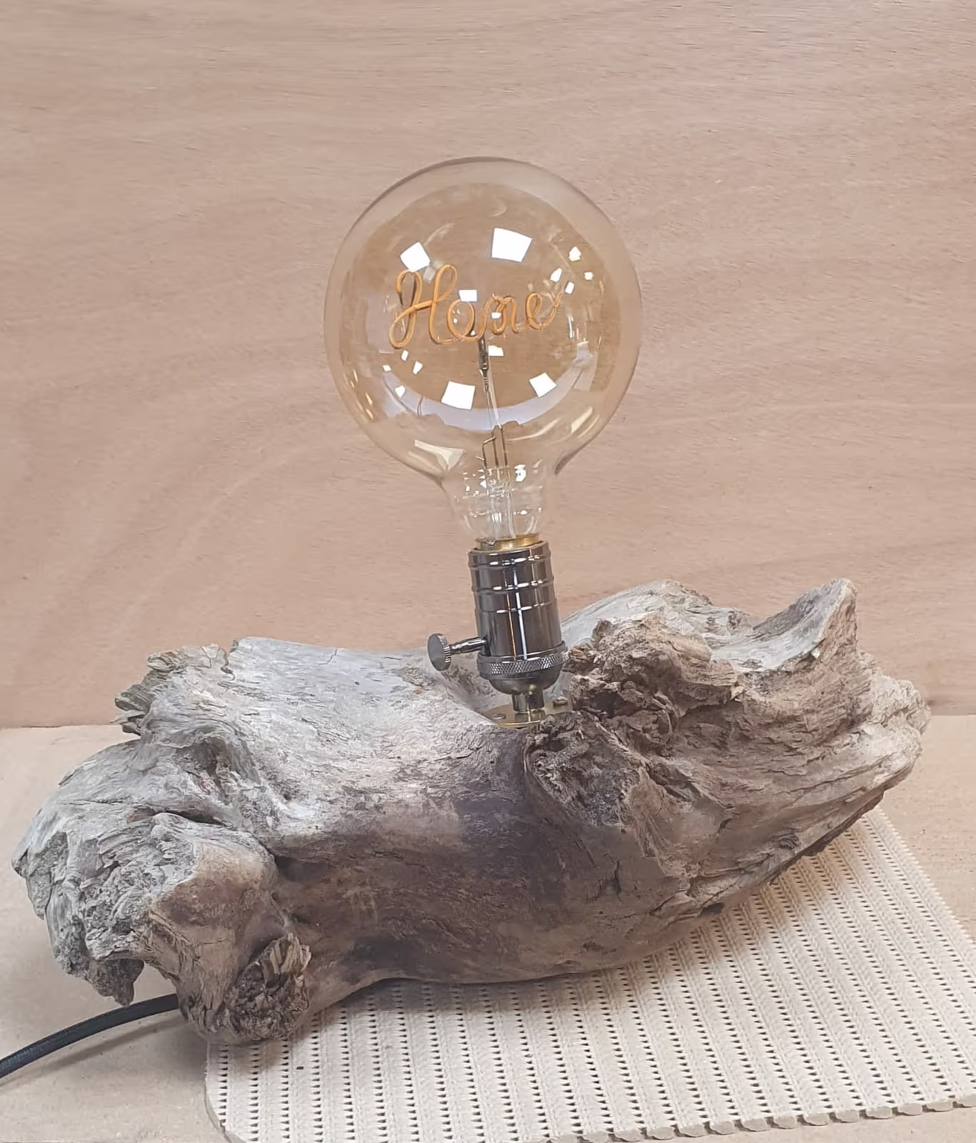 Lampe avec un pied horizontal en bois flotté et une ampoule à filament avec le mot 'HOME'.