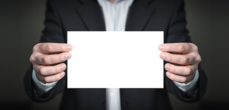 Person in suit holding a blank white card with both hands in front of a dark background.