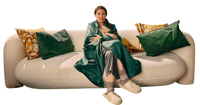 Imaginea prezintă o femeie care are simptome de răceală și gripă, este învelită cu o pătură verde și stă pe o canapea.