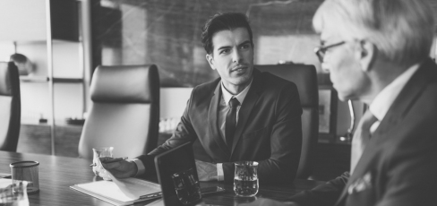 Black and white photo of two men in suits discussing business at a conference table.