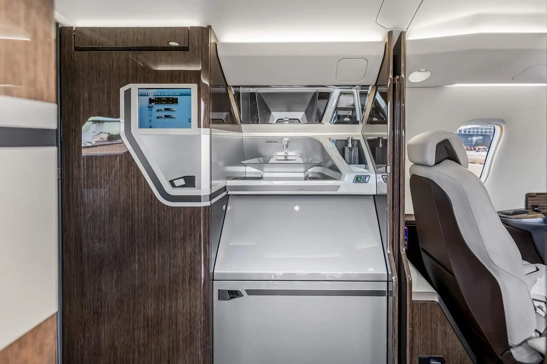 The galley of a private jet with modern appliances, a small screen, and dark wood paneling.