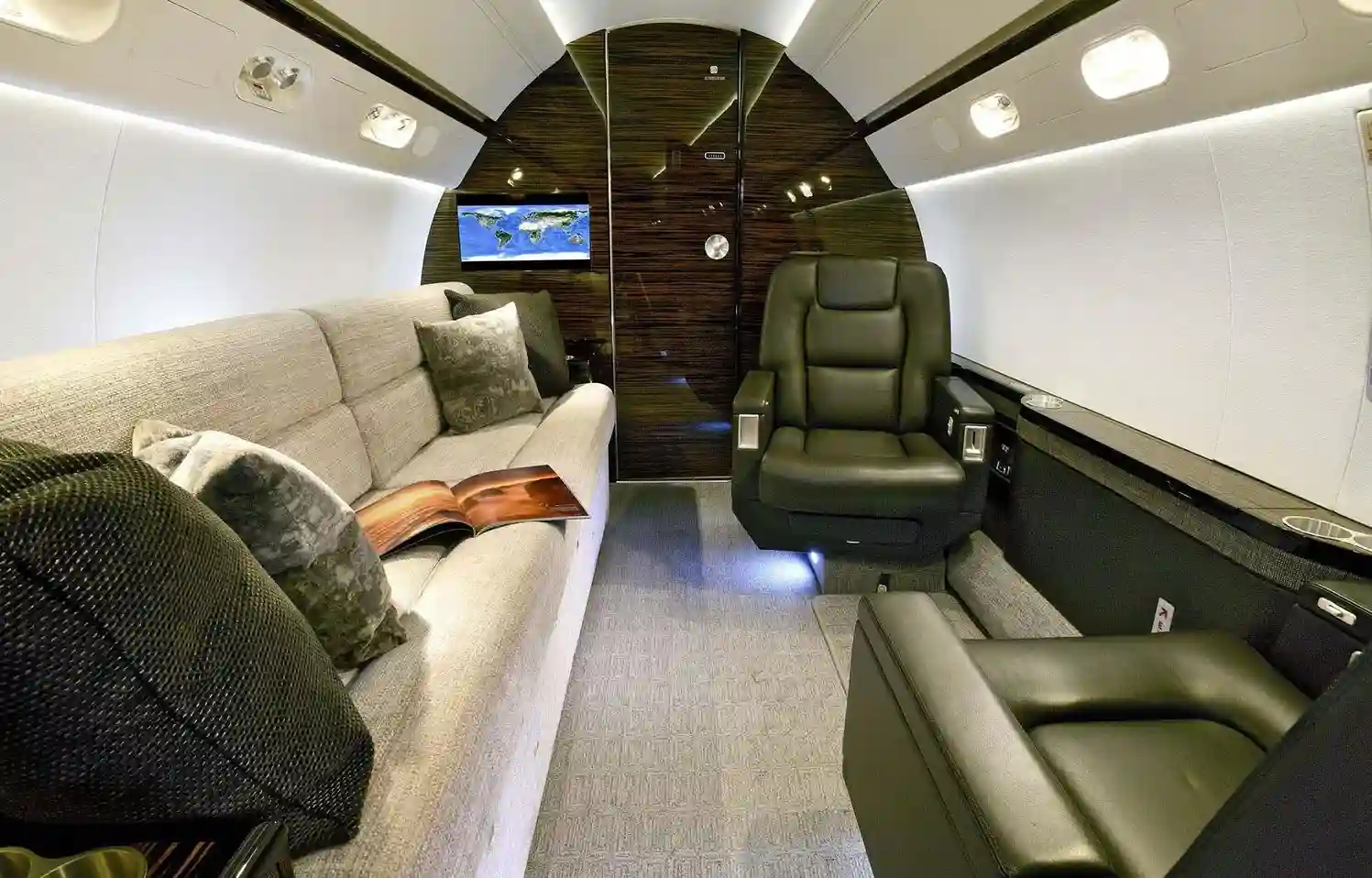 Luxurious private jet interior with a light-colored couch, black leather seats, and wood paneling.