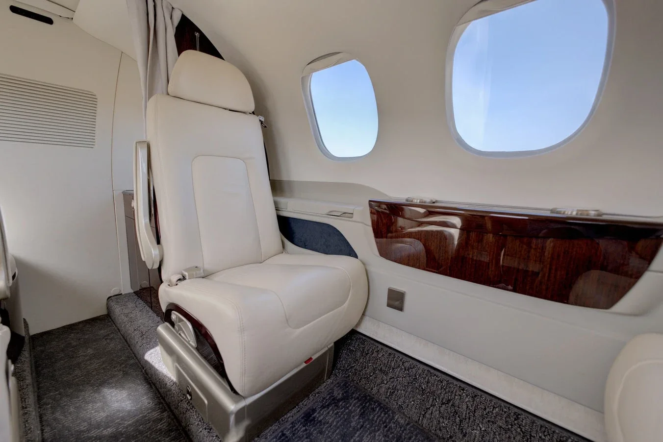 Cream leather single seat in a private jet cabin beside two windows and a dark wood panel.