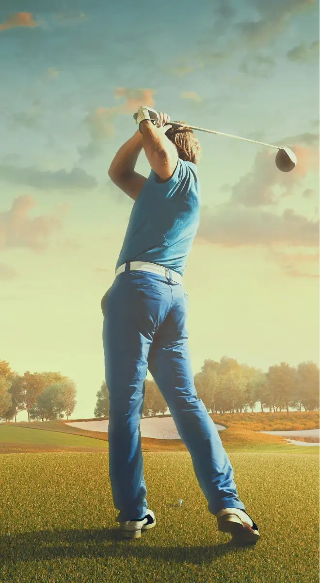 Golfer in a blue shirt and pants mid-swing on a sunny, well-maintained golf course.