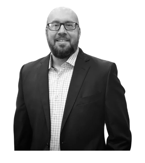 Black and white portrait of a smiling man with a beard and glasses in a suit jacket.