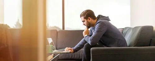 A man in a white shirt is smiling while talking on a phone. He is seated in a modern, well-lit office environment.