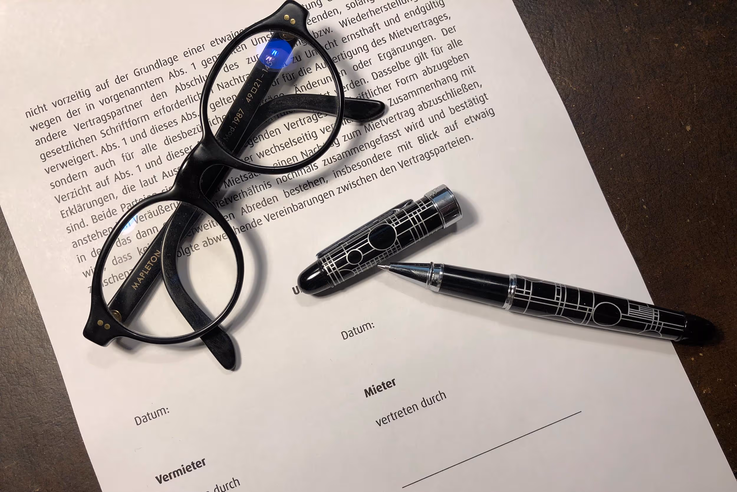 Brille und Schreiber auf dem letzten Blatt eines Vertrags. Der Schreiber ist offen, der Vertrag soll unterschrieben werden.