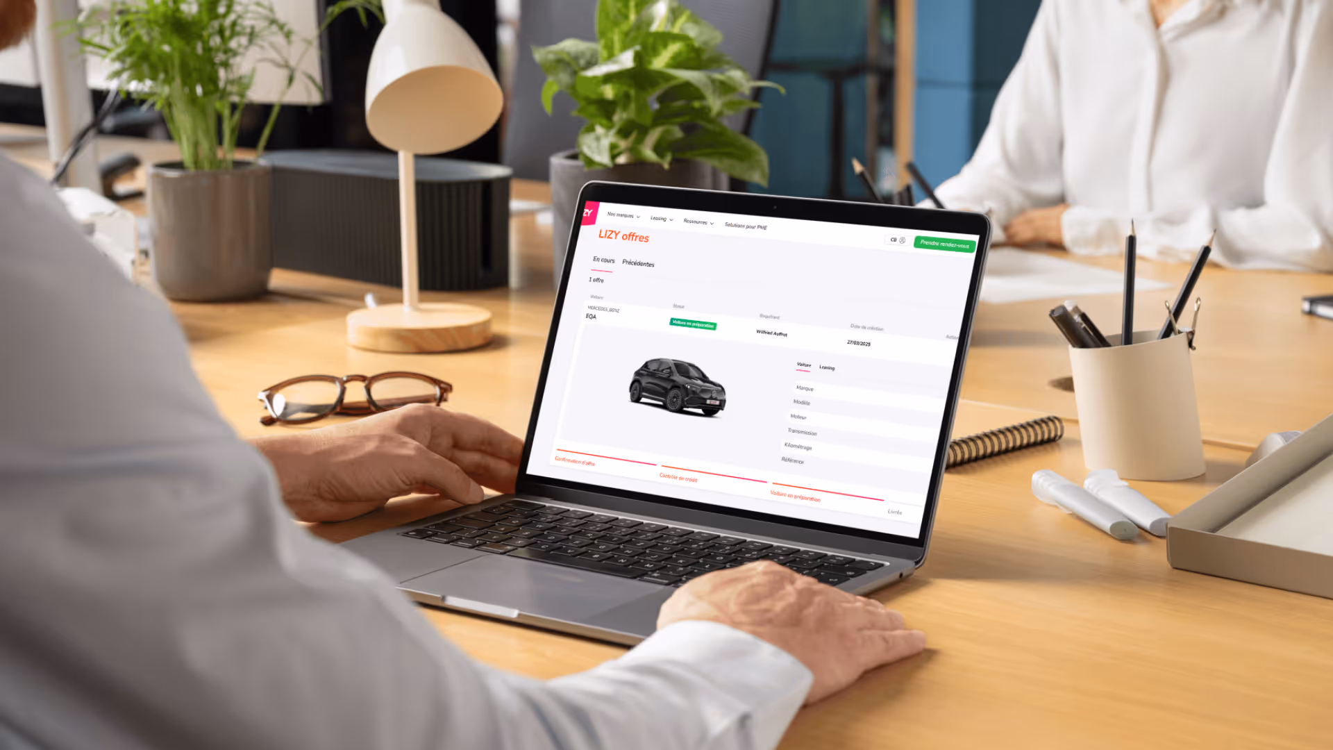 Persoon die op een laptop kijkt met een scherm dat een autolease-aanbieding van Mercedes-Benz EQA toont in een kantooromgeving.