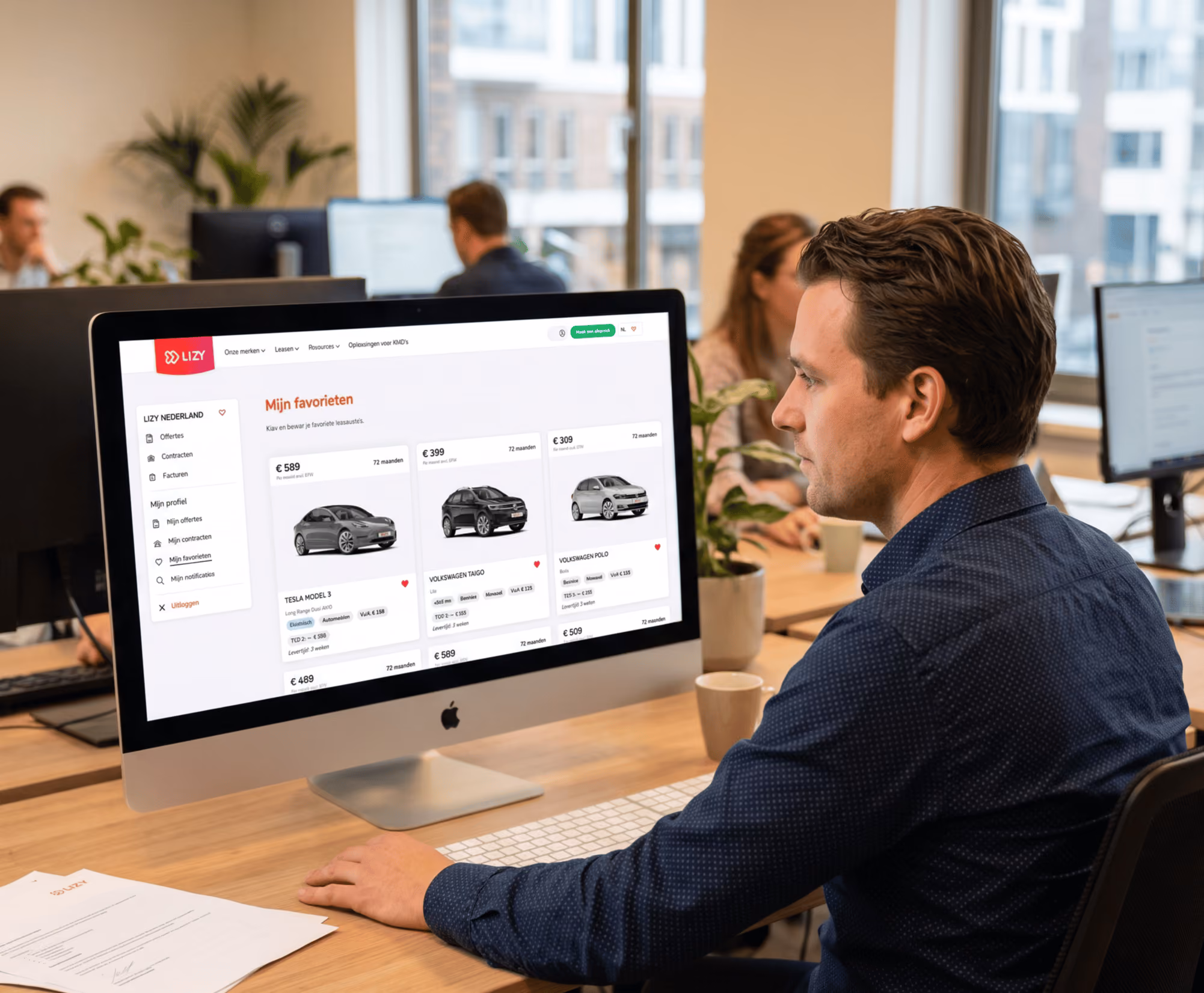 Man zit aan bureau en beheert zijn wagenpark via MyLIZY (online wagenparkbeheer platform van LIZY) op een iMac in een moderne kantoorruimte.