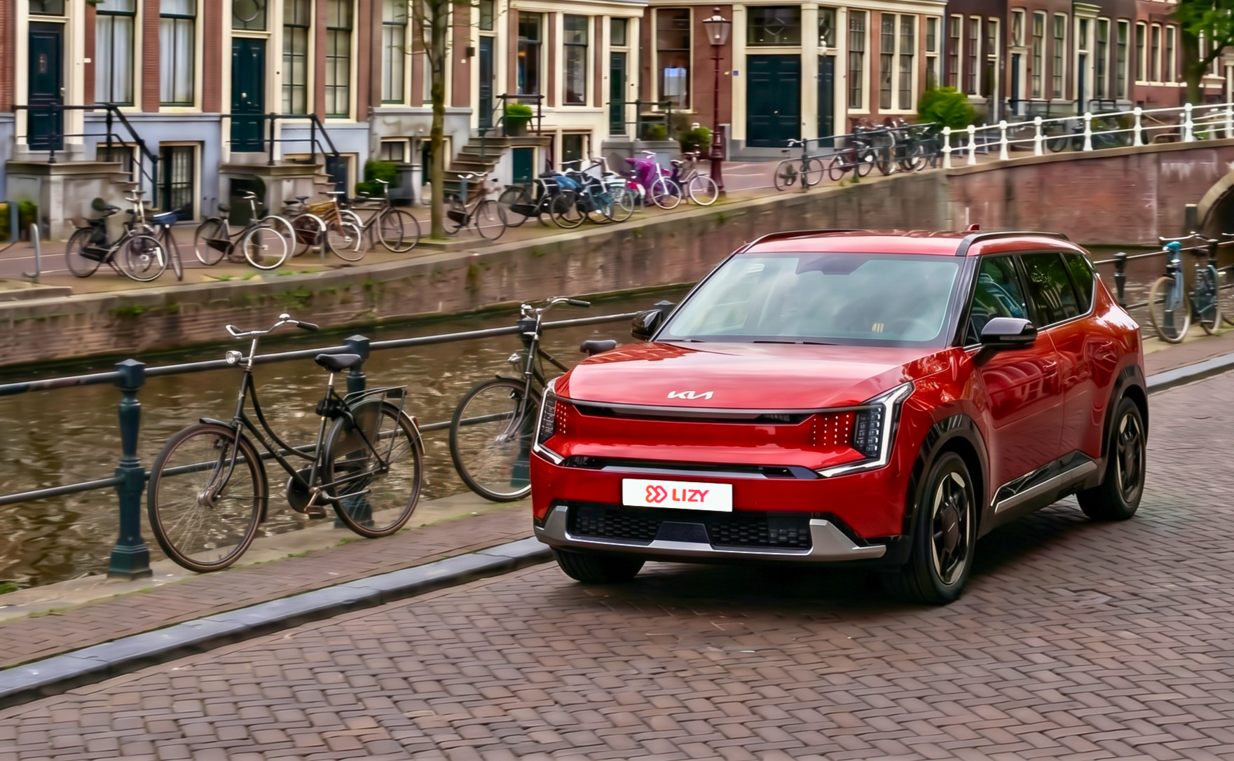 Een jong gebruikte rode KIA EV3 van LIZY geparkeerd langs een gracht in Amsterdam met fietsen en grachtenpanden op de achtergrond.