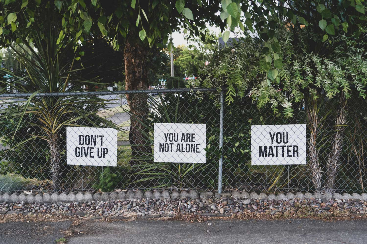 Signs behind a fence that say Don't Give Up, You Are Not Alone, and You Matter