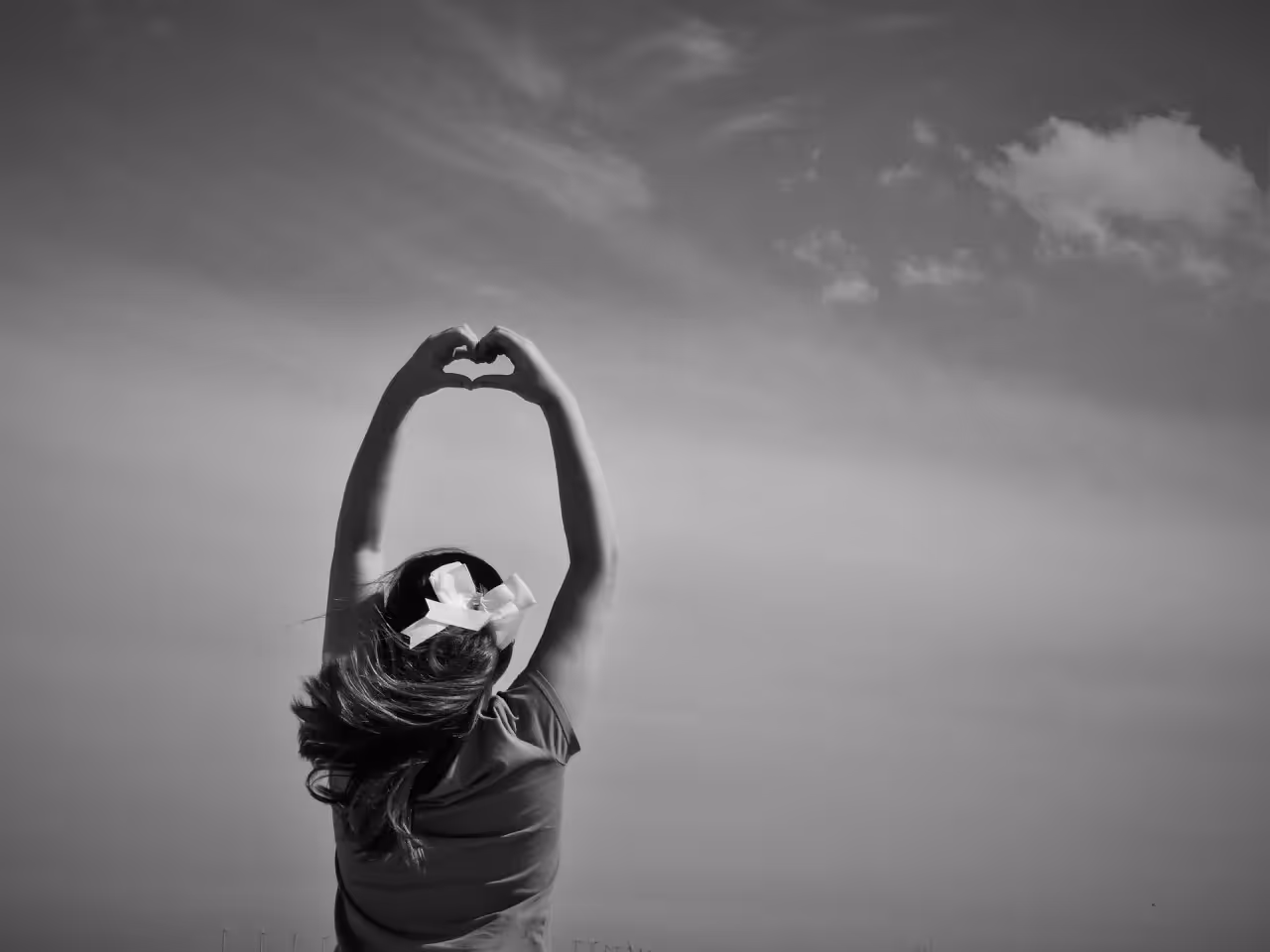 Woman holding hands up towards the sky in the shape of a heart