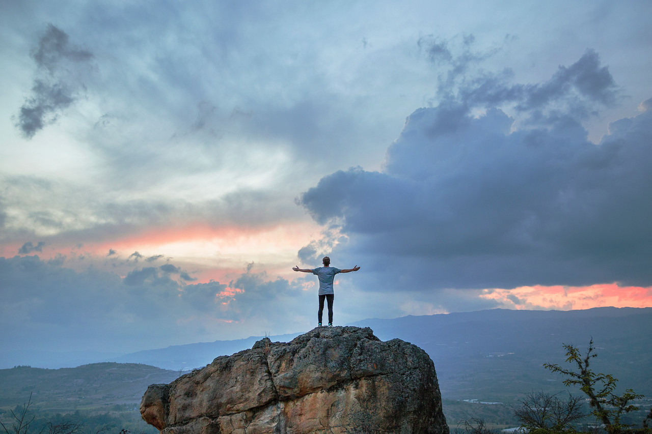 Person standing on a large rock with their holding their hands out
