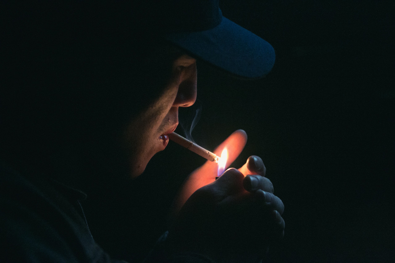 A person lighting a cigarette in their mouth.