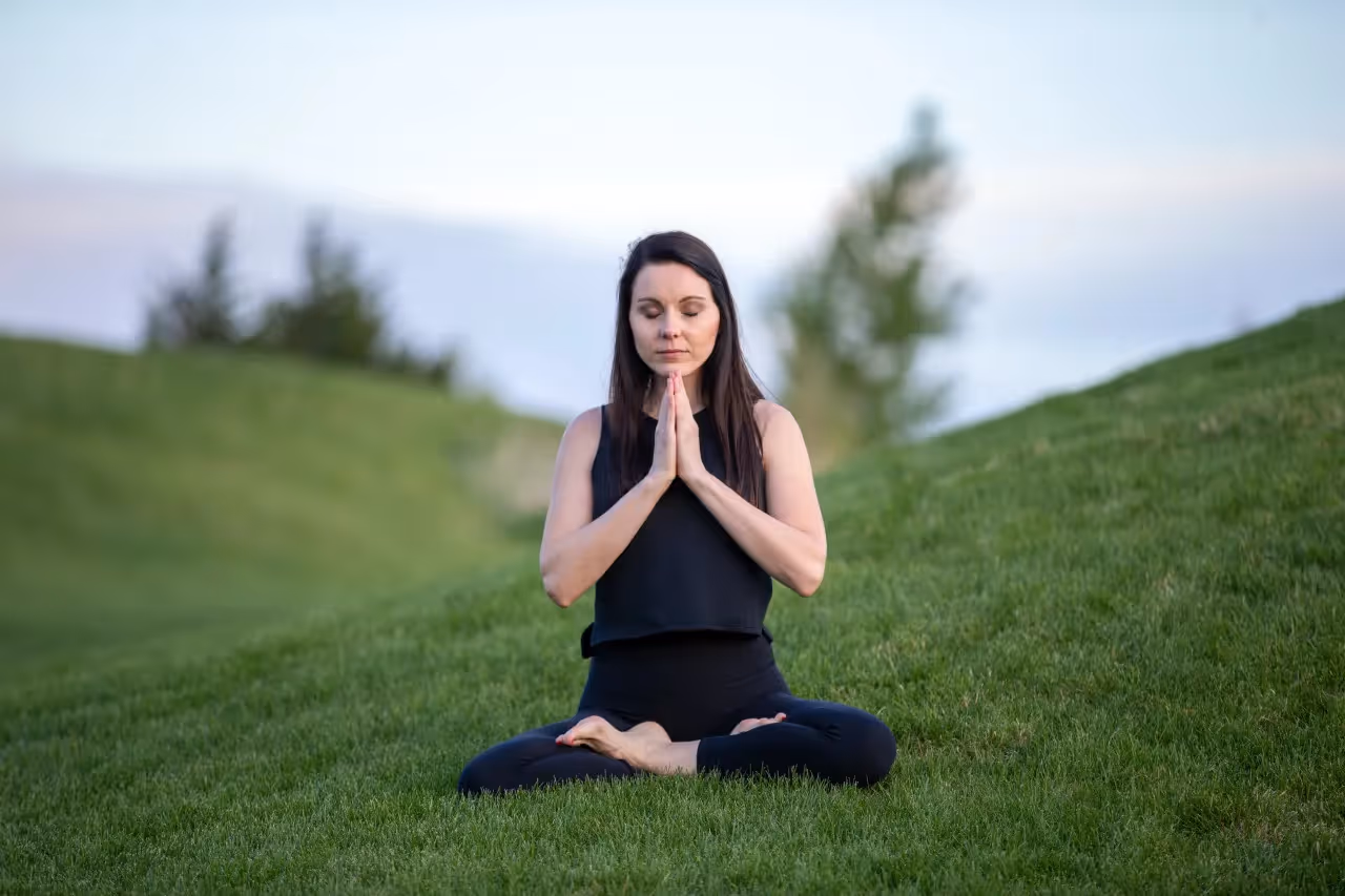 A woman meditating on a grass hill