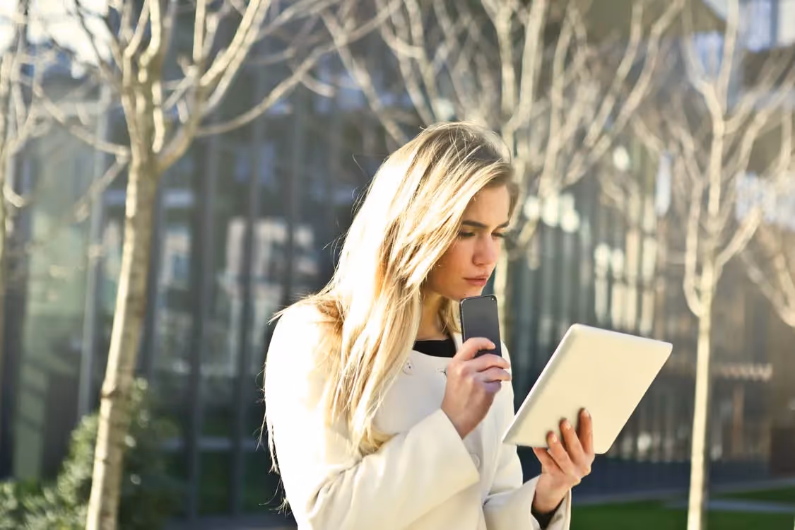 Girl holding her cell phone to her chin and holding a tablet in her other hand