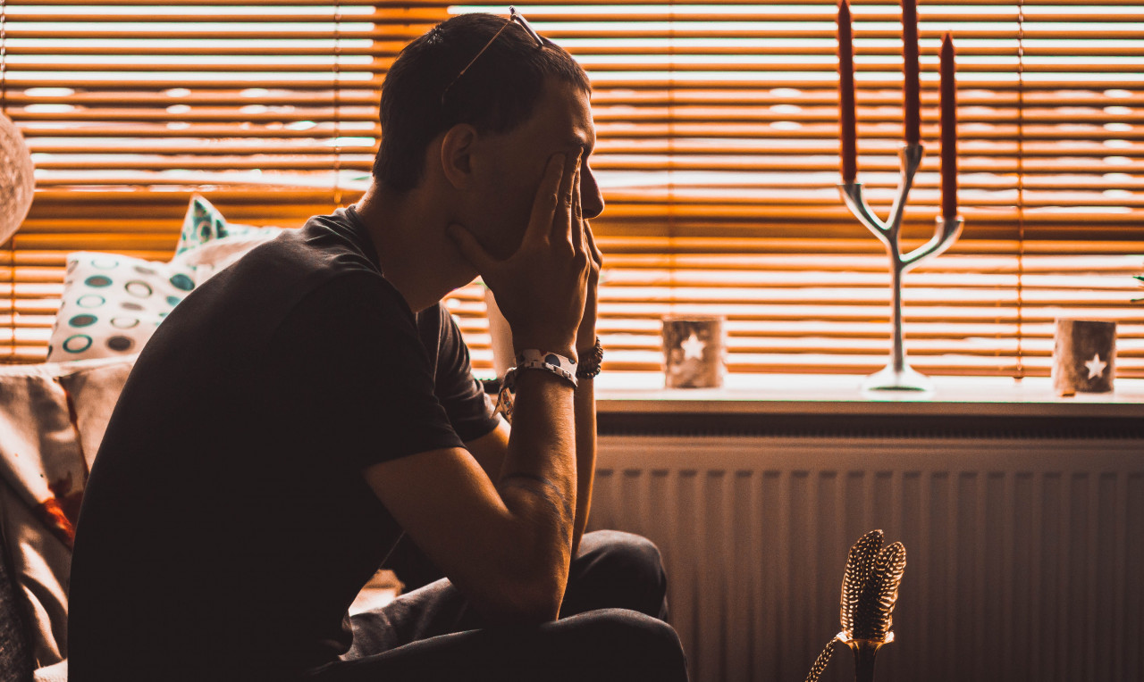 Man sitting on a couch in a room with his fingers covering his eyes