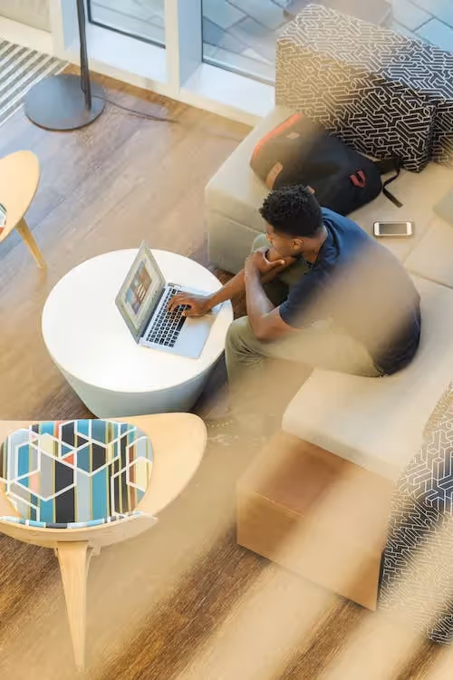 Man Using Gray Laptop While Sitting on Beige Sofa