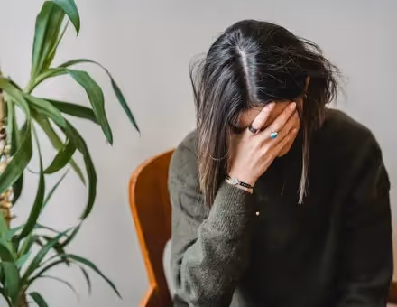 Woman holding her head down with her hand covering her face.