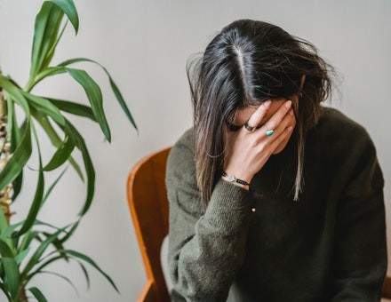 Woman holding her head down with her hand covering her face.