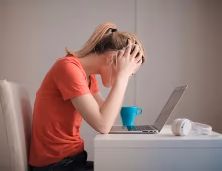 Woman sitting at a desk in front of a computer with her hands on her head.