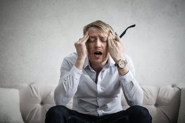 Man sitting on a couch with his hands on his forehead.
