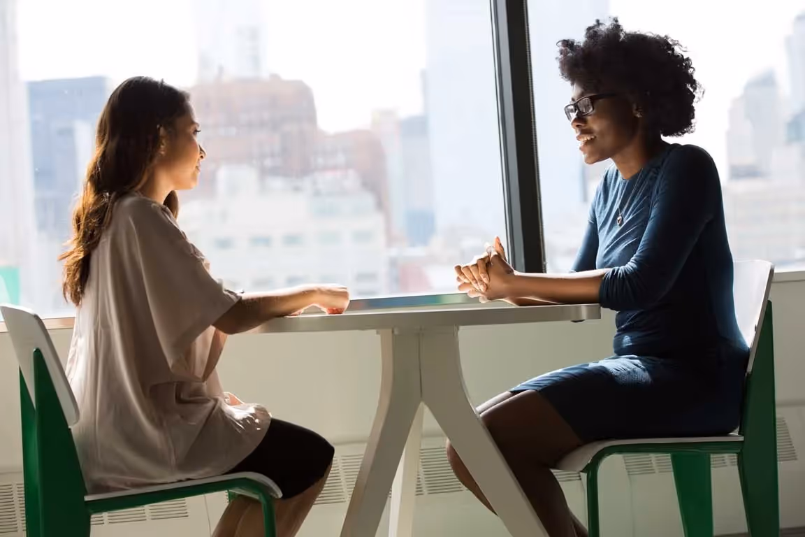 two people talking at a table next to a window