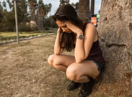 Woman leaning up against a tree with her hands on her head