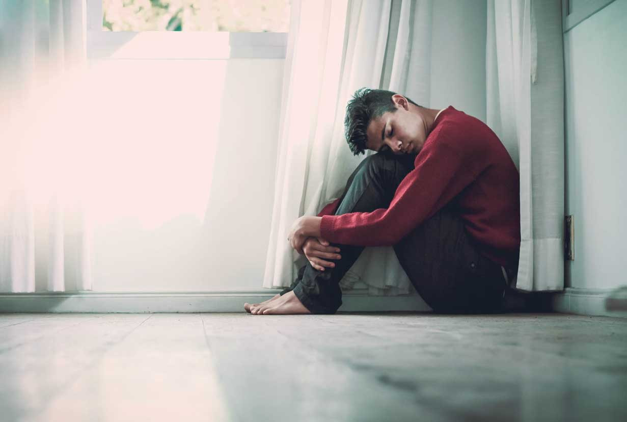 Person sitting on the floor with their arms holding their legs and resting the side of their face on their knees.