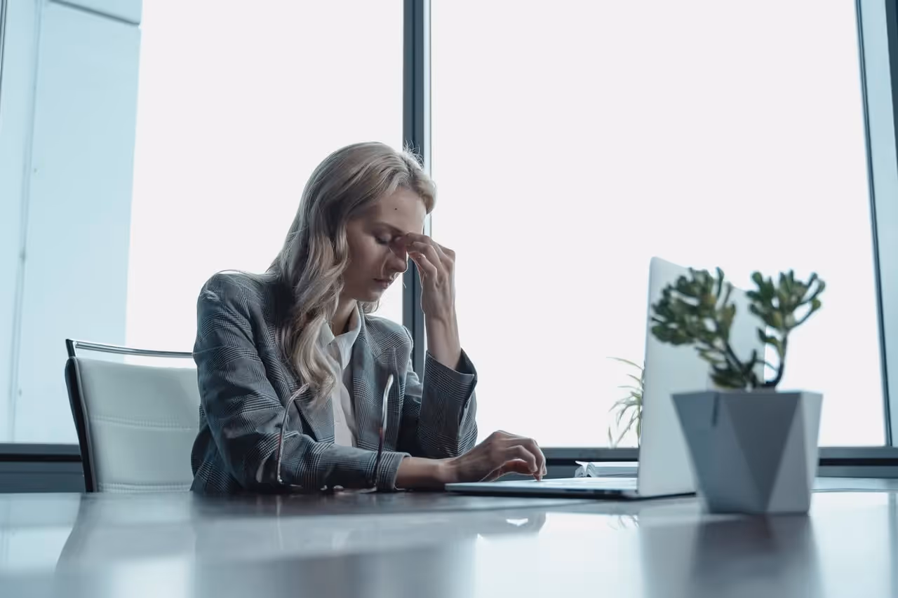 A woman sitting at her computer holding her fingers between her eyes