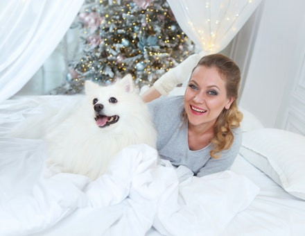 Woman laying on a bed with a white dog.