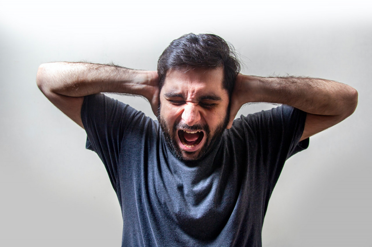 Man in a blue shirt yelling while covering his ears