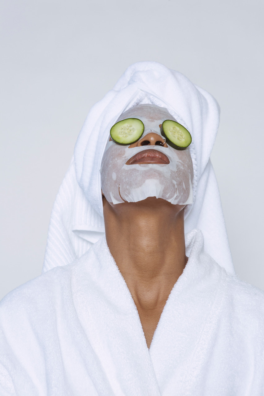 Woman with a sheet mask on her face and cucumbers over her eyes