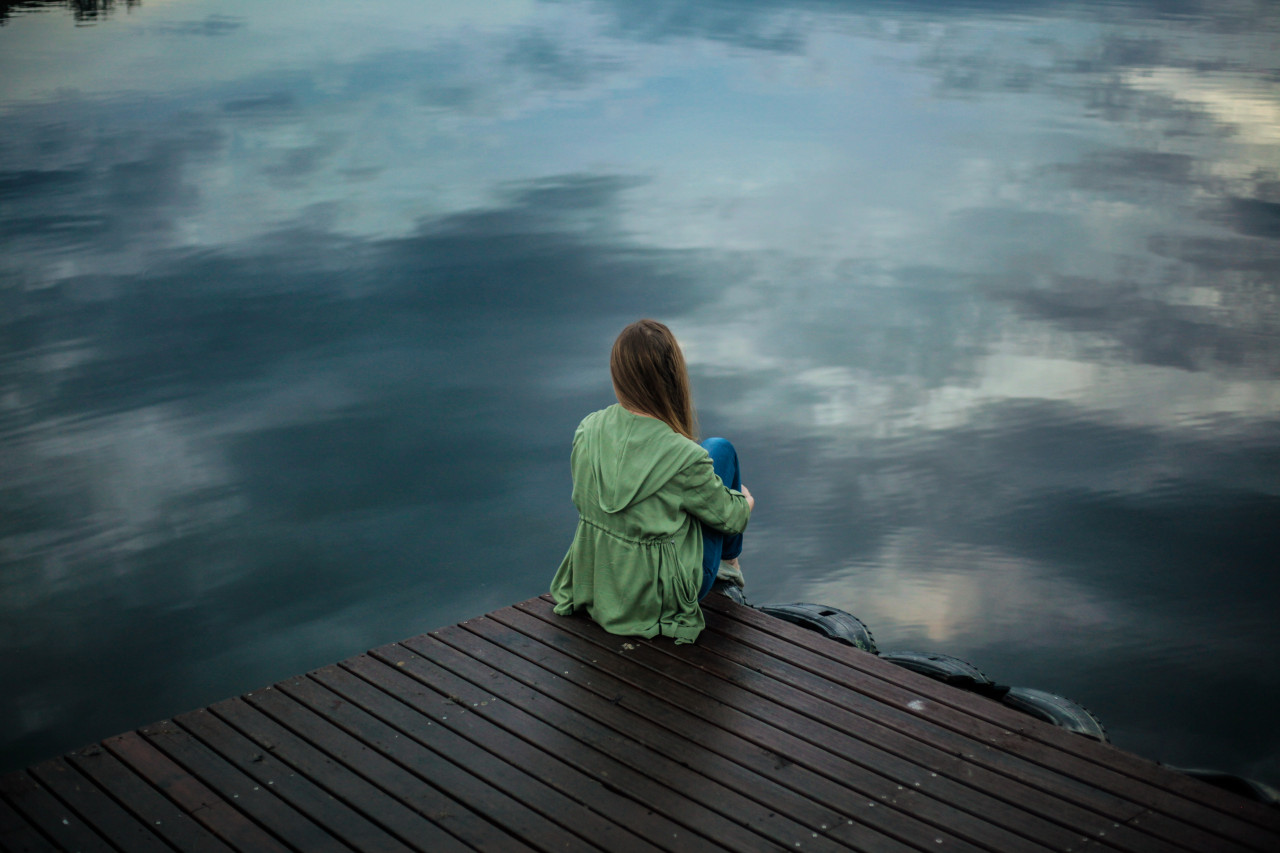 Woman sitting on the edge of a dock overlooking the water