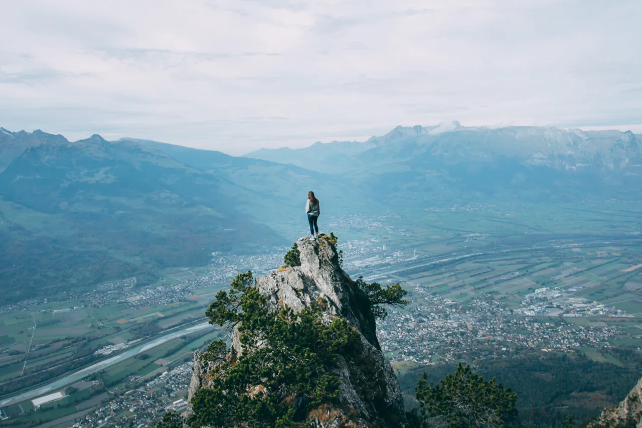 Woman standing at the top of a rock mountain overlooking the land.