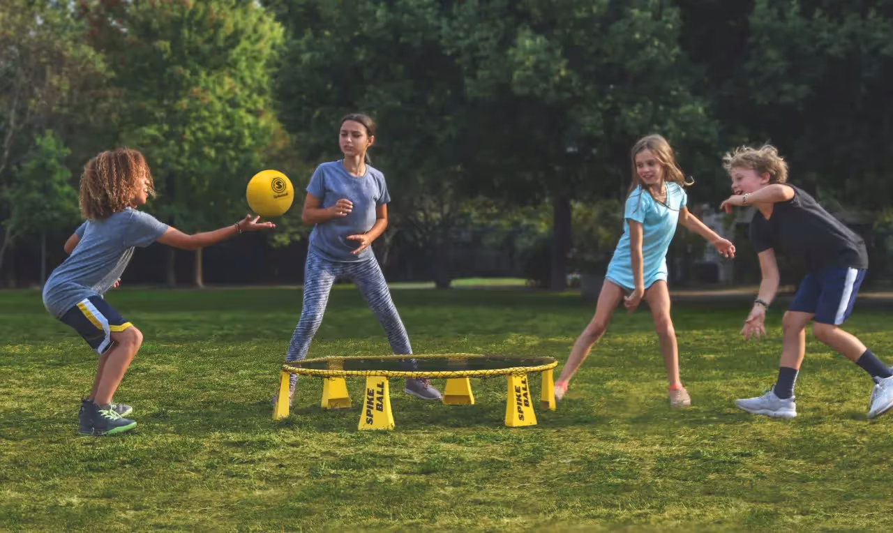 Four kids playing a game called spike ball outside.