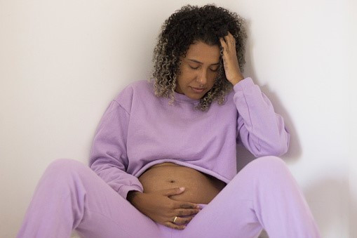 pregnant woman leaning up against the wall with one hand on her head and the other hand on her belly.