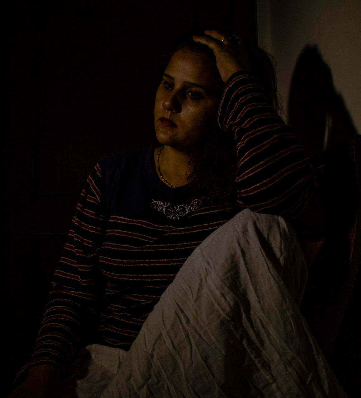 Woman sitting in a dark room with her hand on her head.