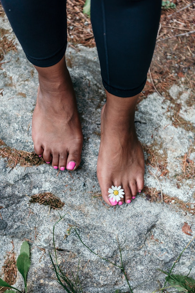 A woman's feet with pink nail polish holding a daisy between her toes.