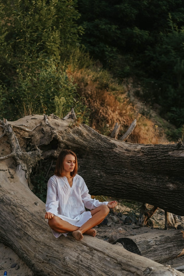 A woman mediating on a fallen tree branch.