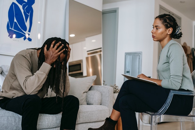 A woman sitting in a chair looking at man holding his head with his hands.