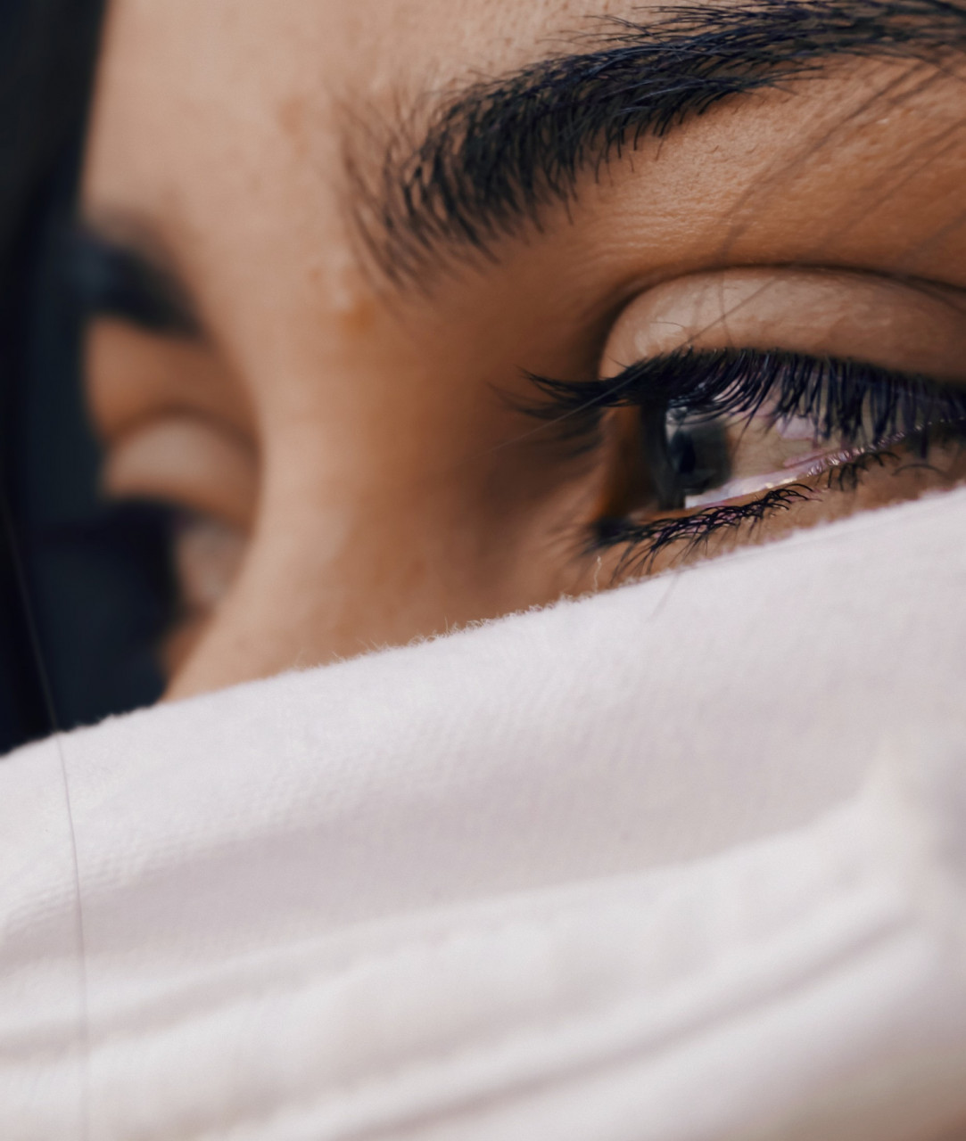 Woman's mouth covered with a white scarf and a tear in her eye